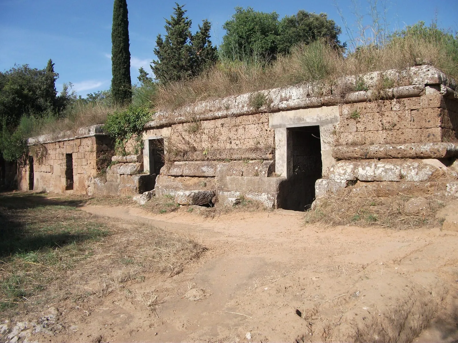 Les façades de tuf des tombes de la nécropole étrusque de la Banditaccia à Cerveteri, le long d'un chemin de terre