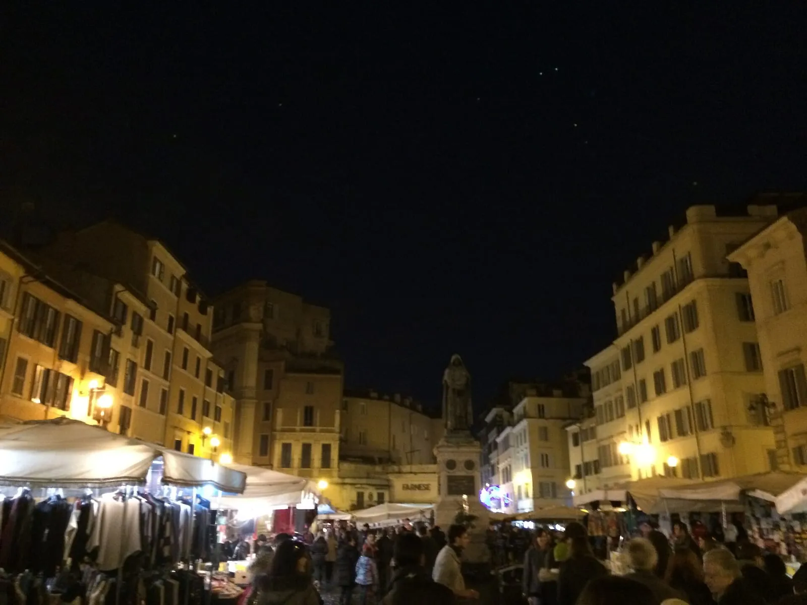La place Campo de' Fiori à Rome la nuit, ses étals de marché éclairés et la foule du soir