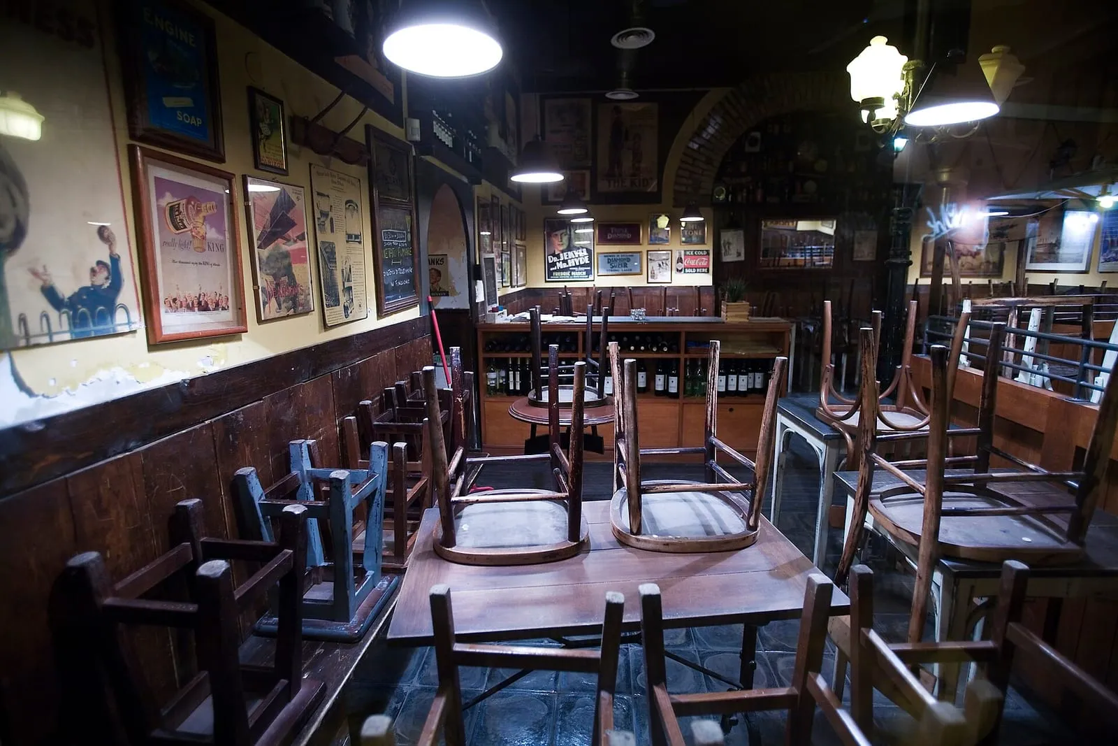 Intérieur d'un restaurant de Trastevere à Rome la nuit, chaises posées sur les tables à l'heure de la fermeture et murs couverts d'affiches anciennes