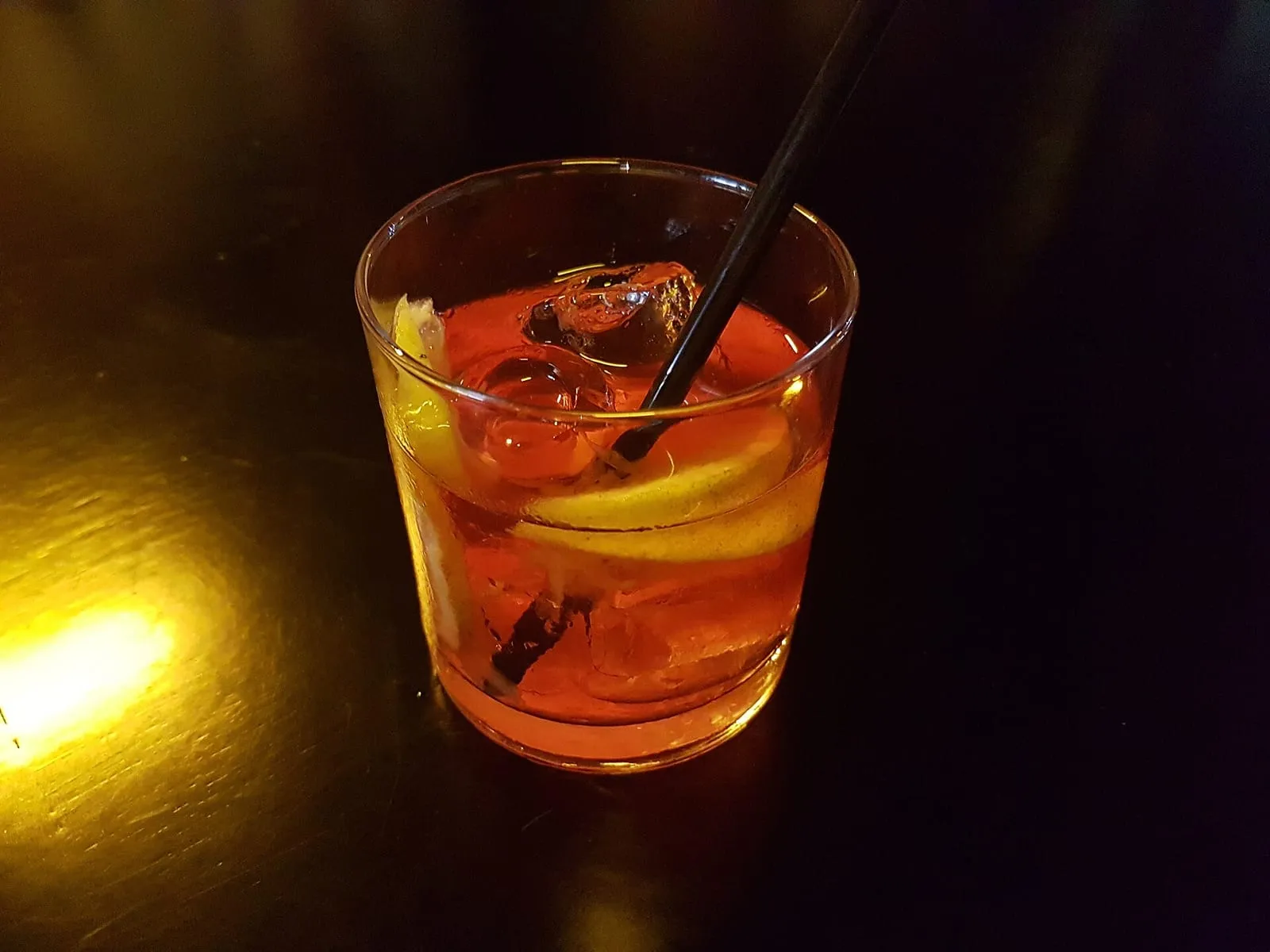 Un Negroni rouge servi dans un verre à fond épais, garni d'une rondelle d'orange