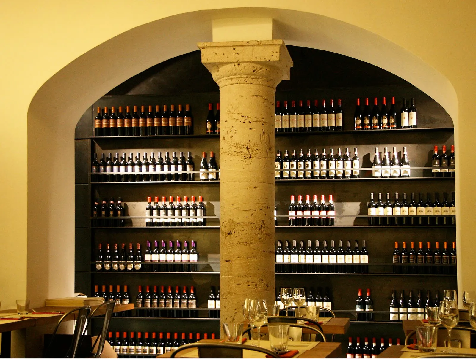 Mur de bouteilles de vin rangées sur des étagères, autour d'une colonne en pierre, dans un bar à vin romain