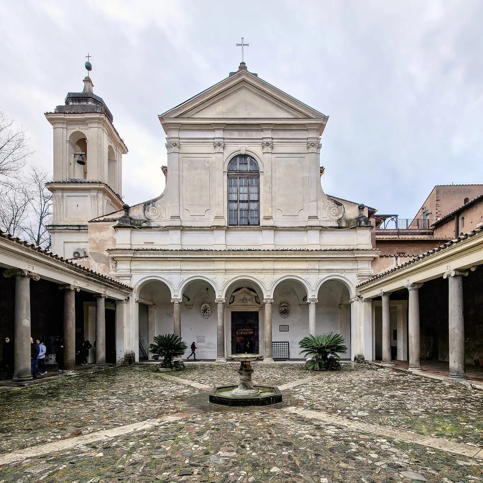 La façade de la basilique Saint-Clément à Rome vue depuis son atrium, avec son portique à colonnes antiques, sa fontaine centrale et le campanile sur la gauche