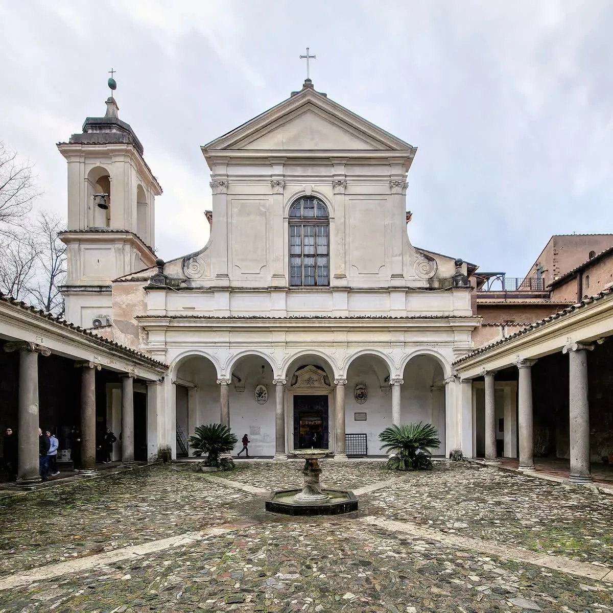 La façade de la basilique Saint-Clément à Rome vue depuis son atrium, avec son portique à colonnes antiques, sa fontaine centrale et le campanile sur la gauche