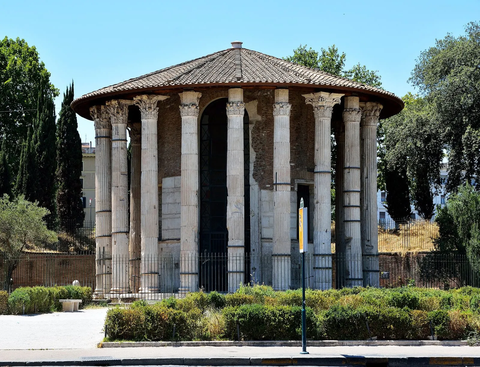 Le temple circulaire d'Hercule Vainqueur au Forum Boarium, ses colonnes corinthiennes et son toit de tuiles, derrière les haies et la grille de la piazza