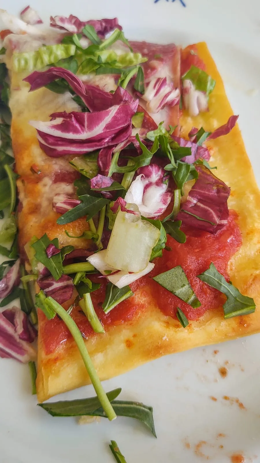 Part de pizza al taglio garnie de roquette et de radicchio, posée sur son papier, prête à être mangée debout