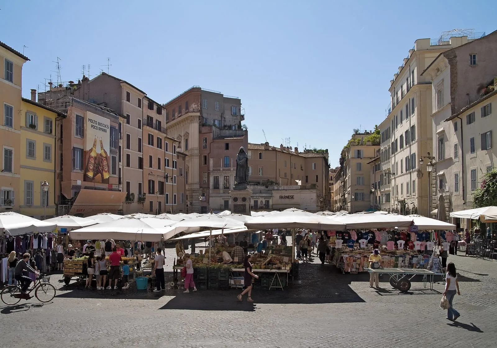 Le marché du Campo de' Fiori à Rome, étals et parasols blancs devant les façades du côté Farnese et la statue de Giordano Bruno