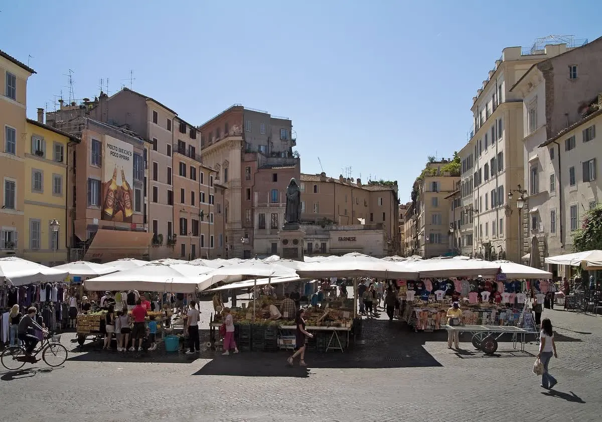 Le marché de Campo de' Fiori à Rome, ses étals de fruits et légumes sous les parasols blancs et la statue de Giordano Bruno
