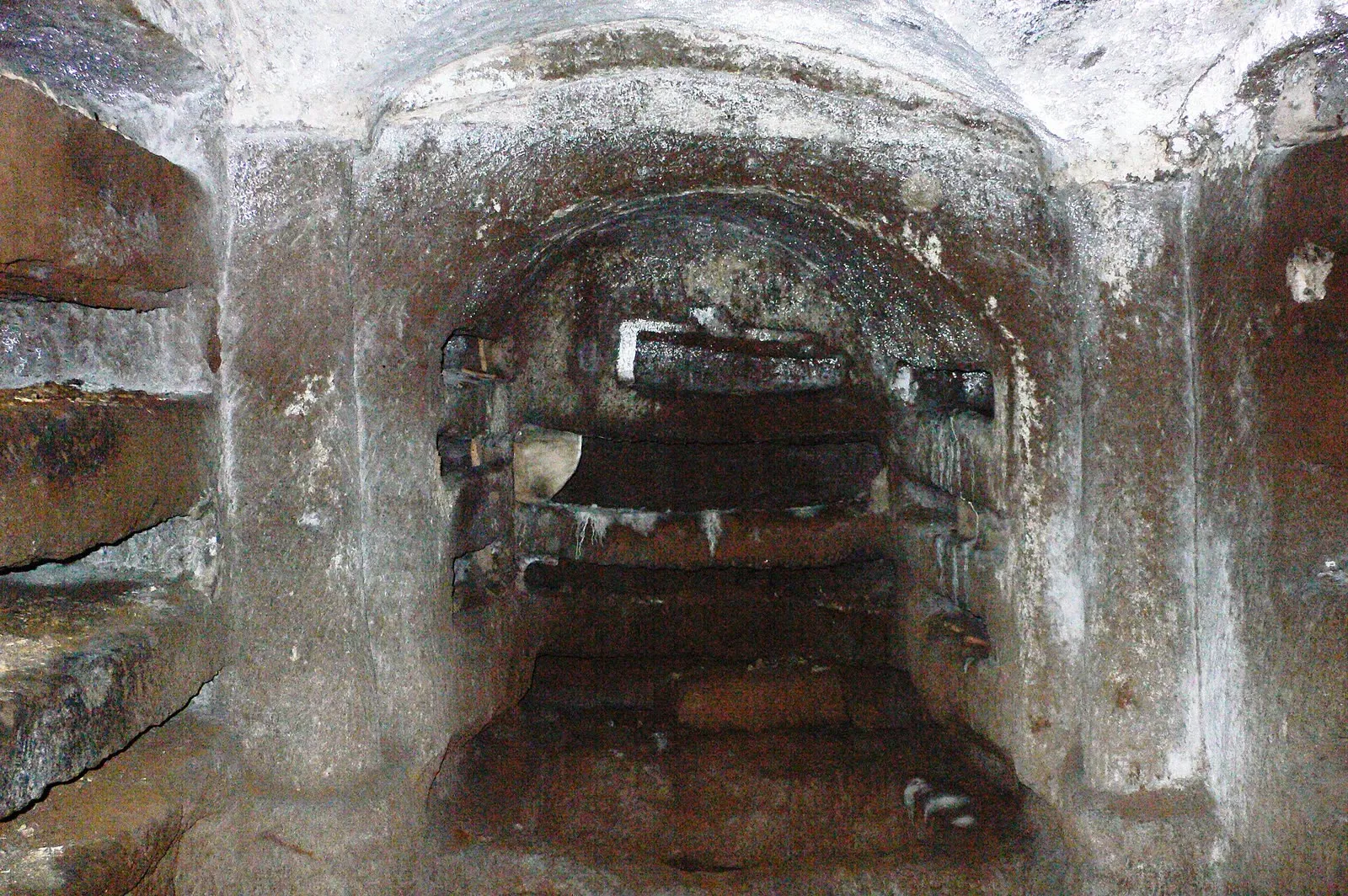 Niches funéraires superposées dans une galerie des catacombes de Domitille, fermées par des dalles, sous une arcade de brique