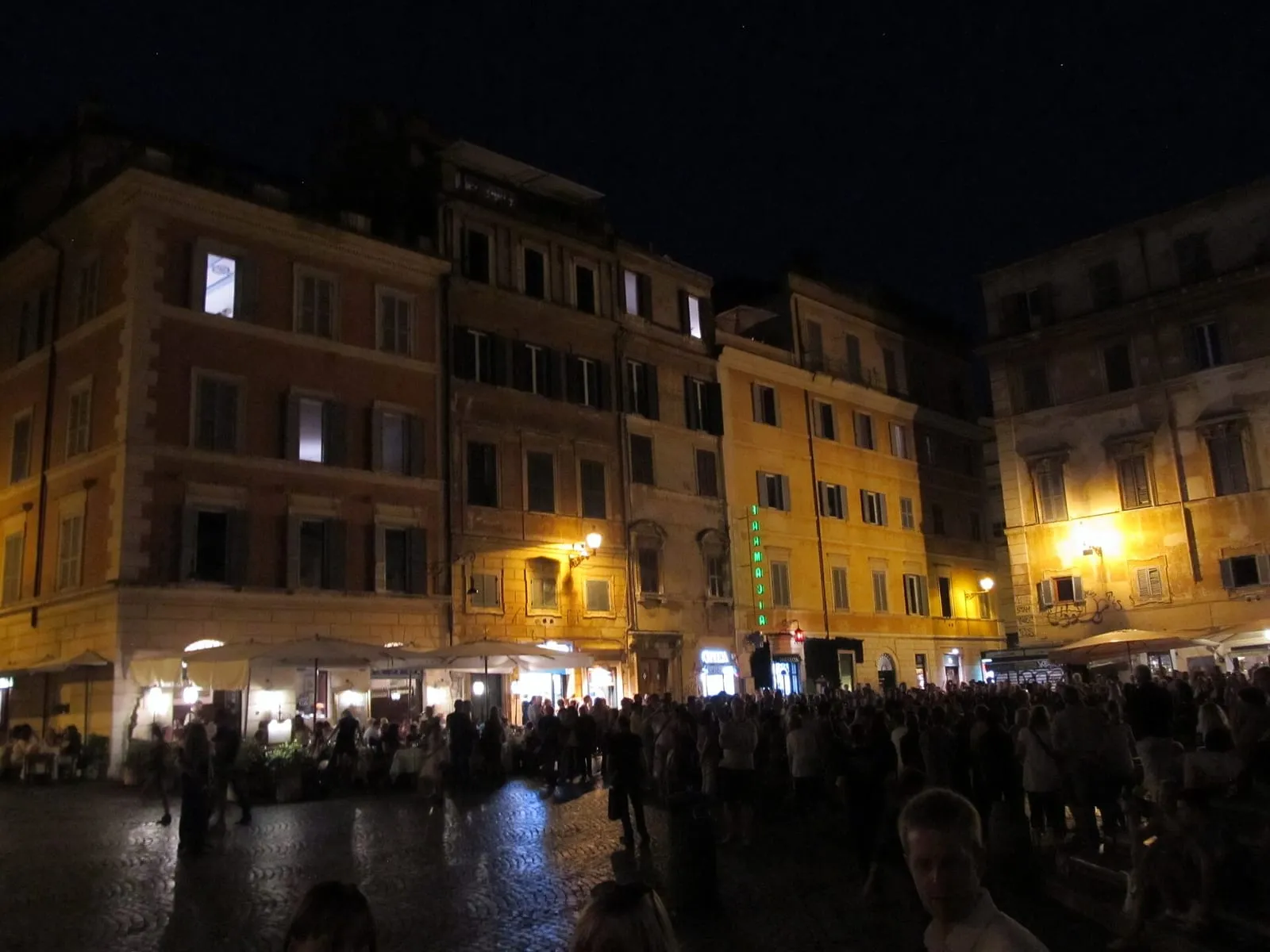 La piazza Santa Maria in Trastevere à Rome la nuit, façades éclairées, terrasses et foule sur les pavés