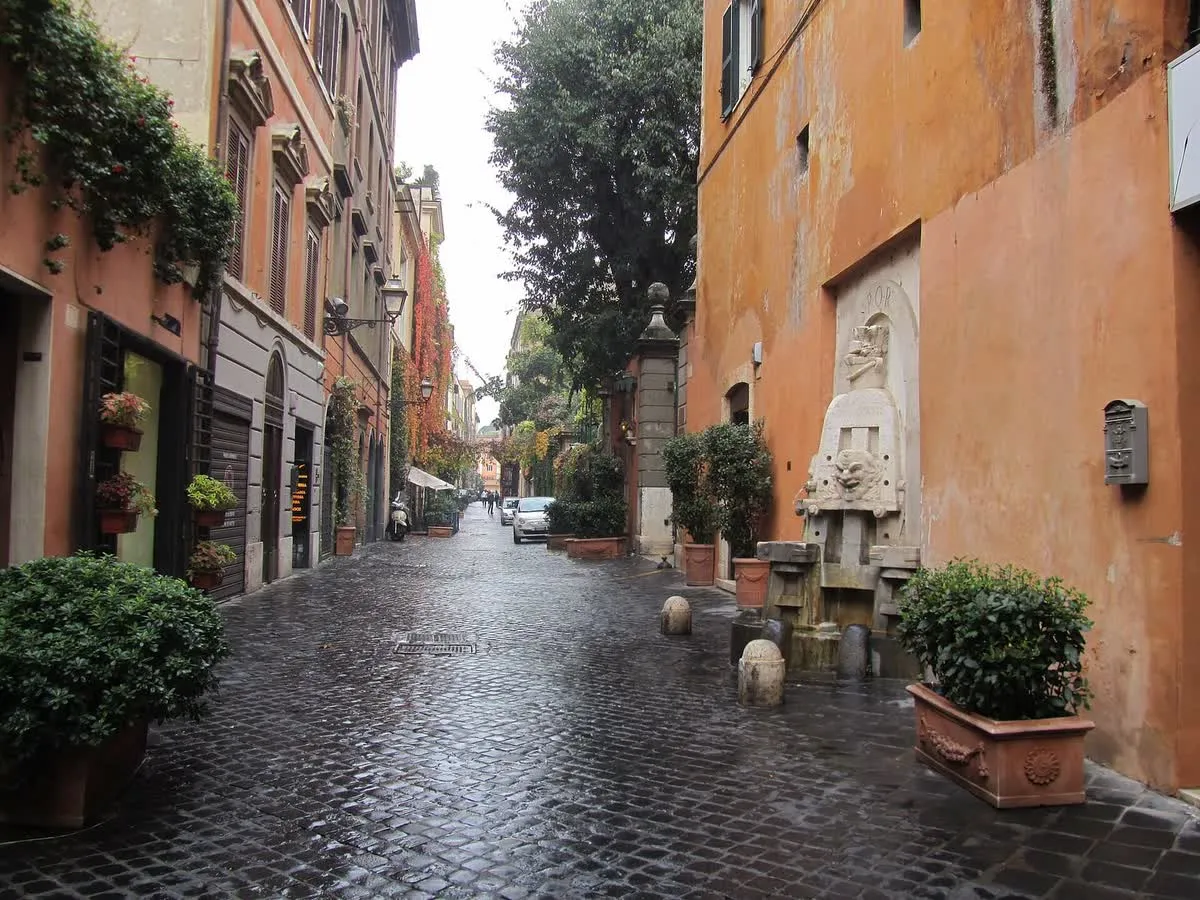 La via Margutta à Rome, rue pavée bordée d'immeubles ocre et de plantes en pot, avec la fontaine des Arts au premier plan à droite