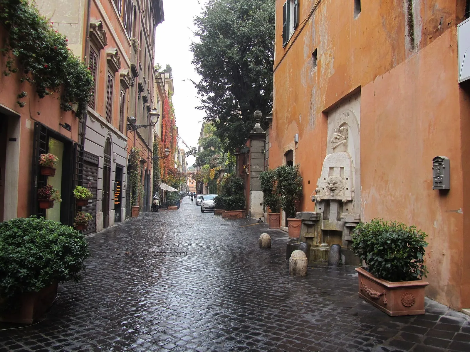 La via Margutta à Rome, rue pavée bordée d'immeubles ocre et de plantes en pot, avec la fontaine des Arts au premier plan à droite