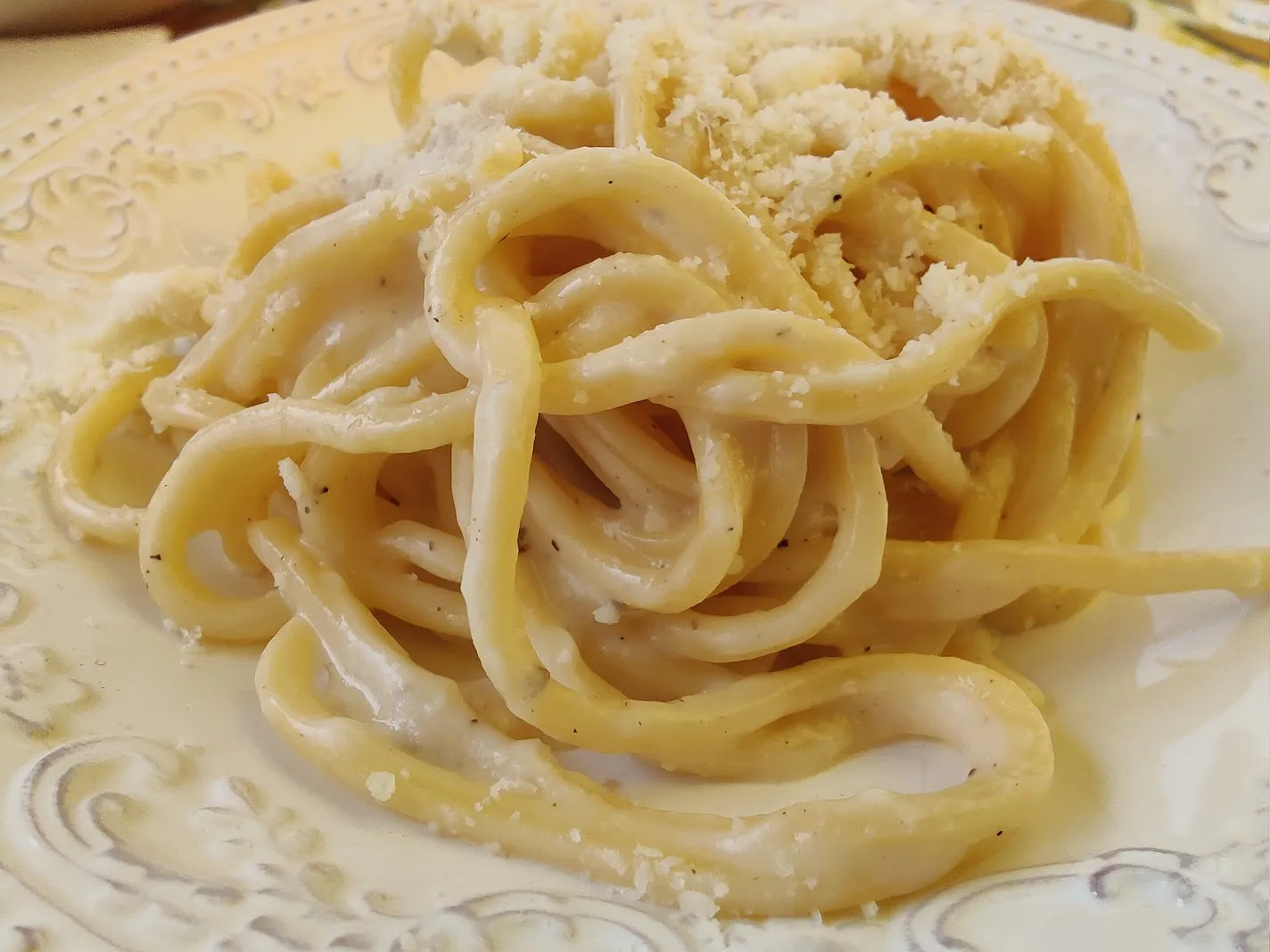 Tonnarelli au pecorino et au poivre, nappés de sauce au fromage râpé dans une assiette claire