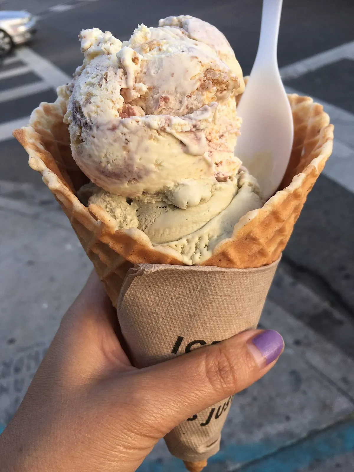 Cornet gaufré garni de trois boules de gelato, tenu à la main dans une rue de Rome