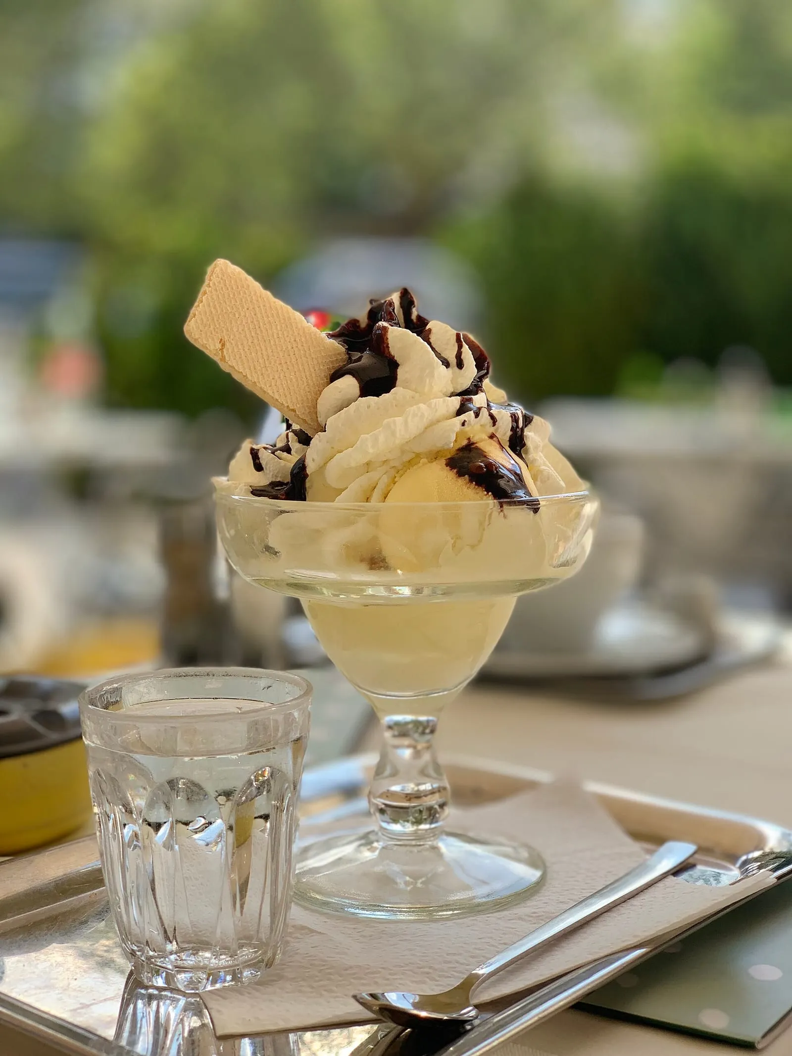 Coupe de glace à la vanille coiffée de chantilly et nappée de sauce au chocolat, servie en terrasse