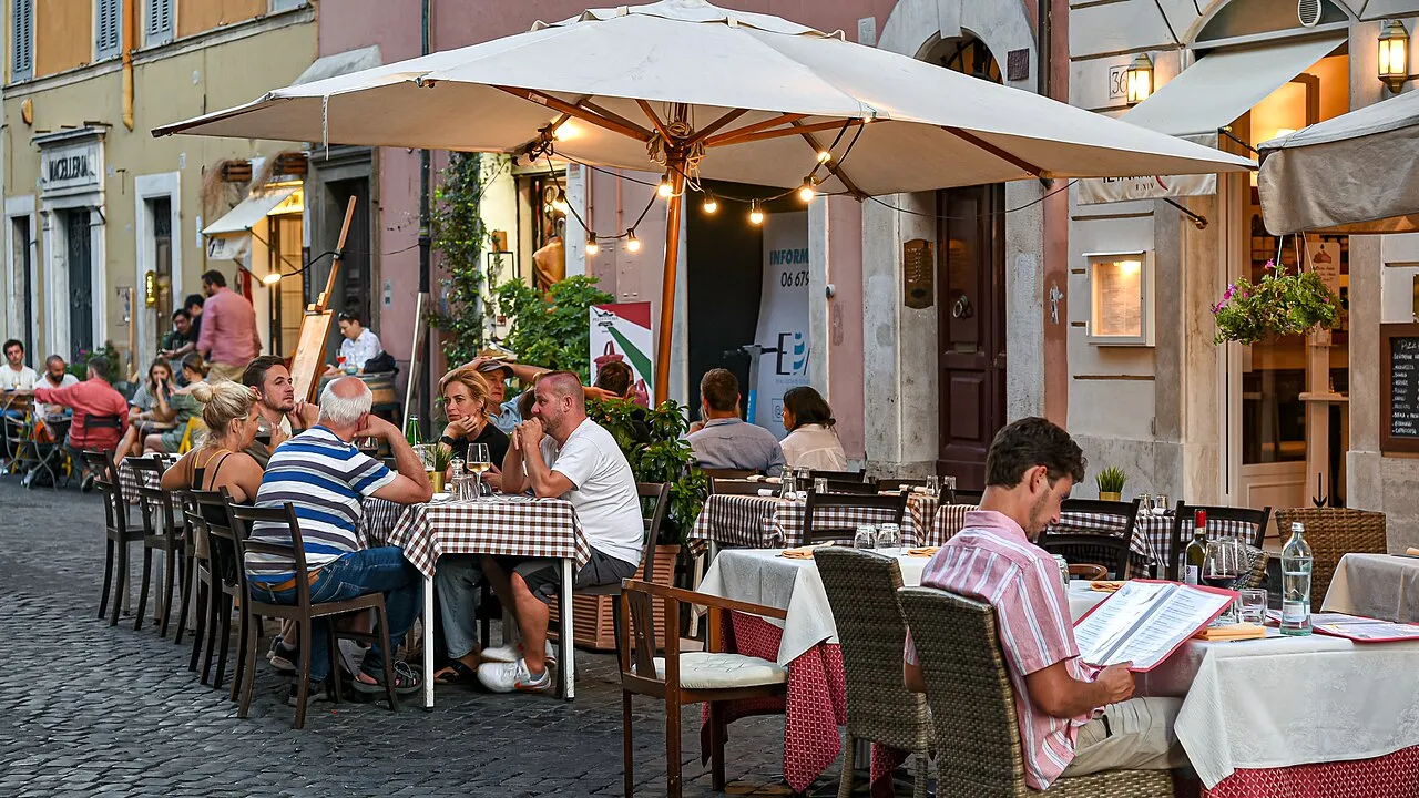 Terrasses de restaurants éclairées de guirlandes le soir dans une rue du Borgo Pio à Rome