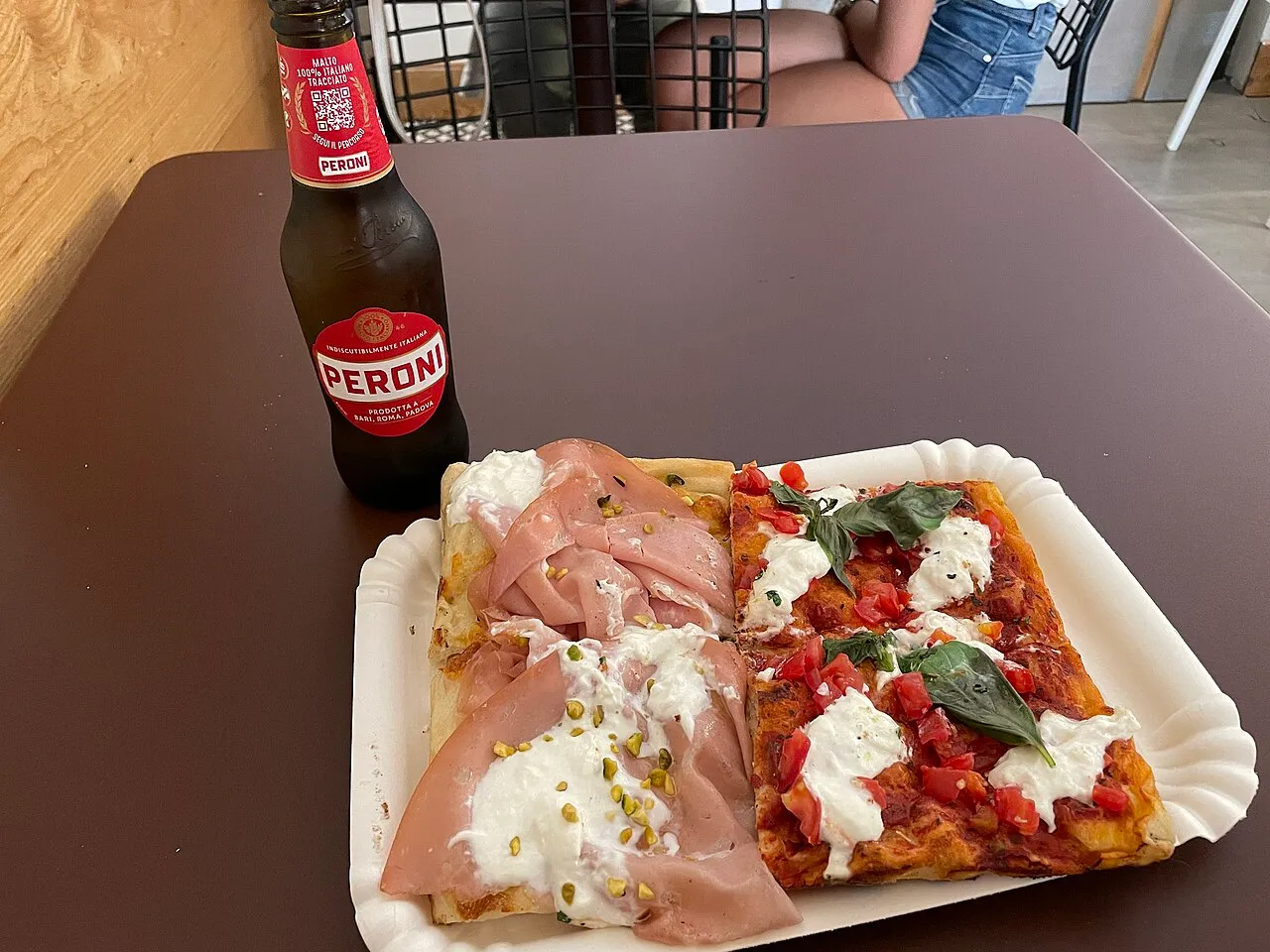 Deux parts de pizza al taglio romaine sur une assiette en carton, accompagnées d'une bière Peroni