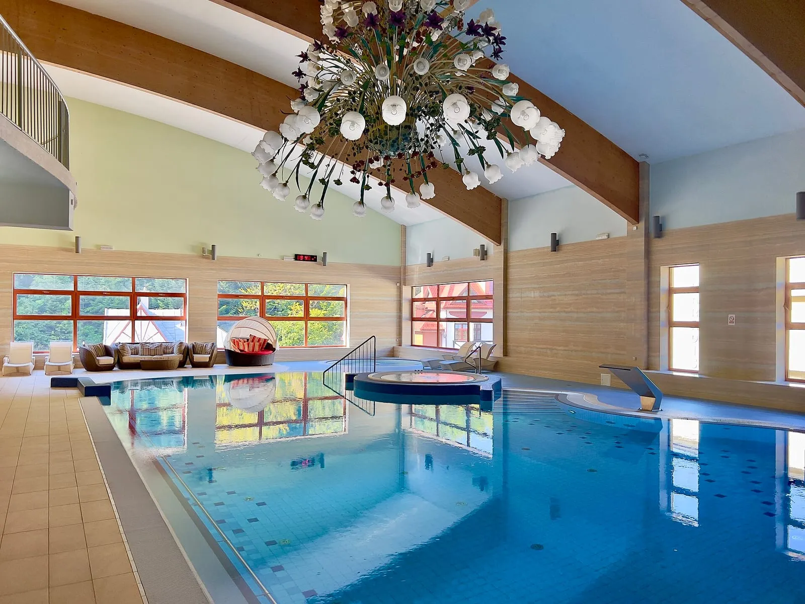 Piscine intérieure d'un spa d'hôtel, bassin au carrelage clair bordé de bains à remous et de baies vitrées sous une charpente de bois