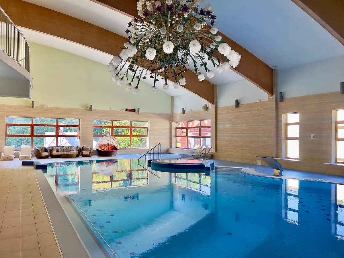 Piscine intérieure d'un spa d'hôtel, bassin au carrelage clair bordé de bains à remous et de baies vitrées sous une charpente de bois