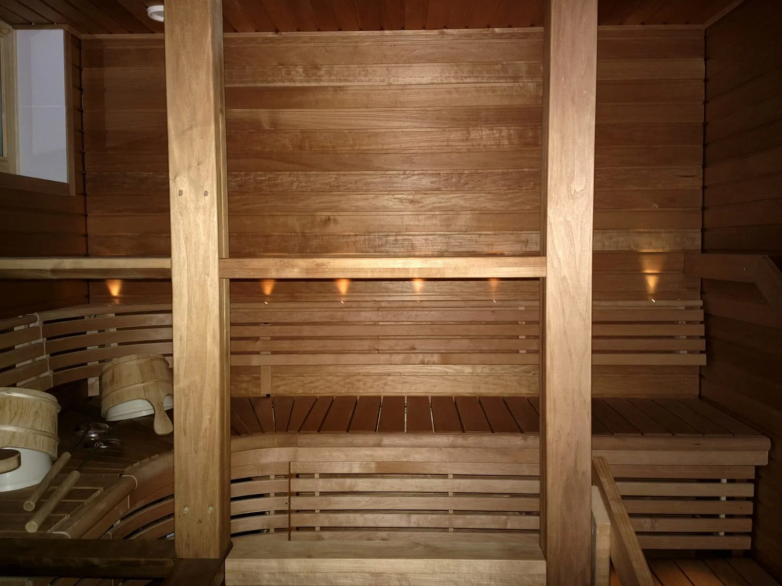 Intérieur d'un sauna finlandais en bois clair, banquettes étagées, seaux et louches posés au sol