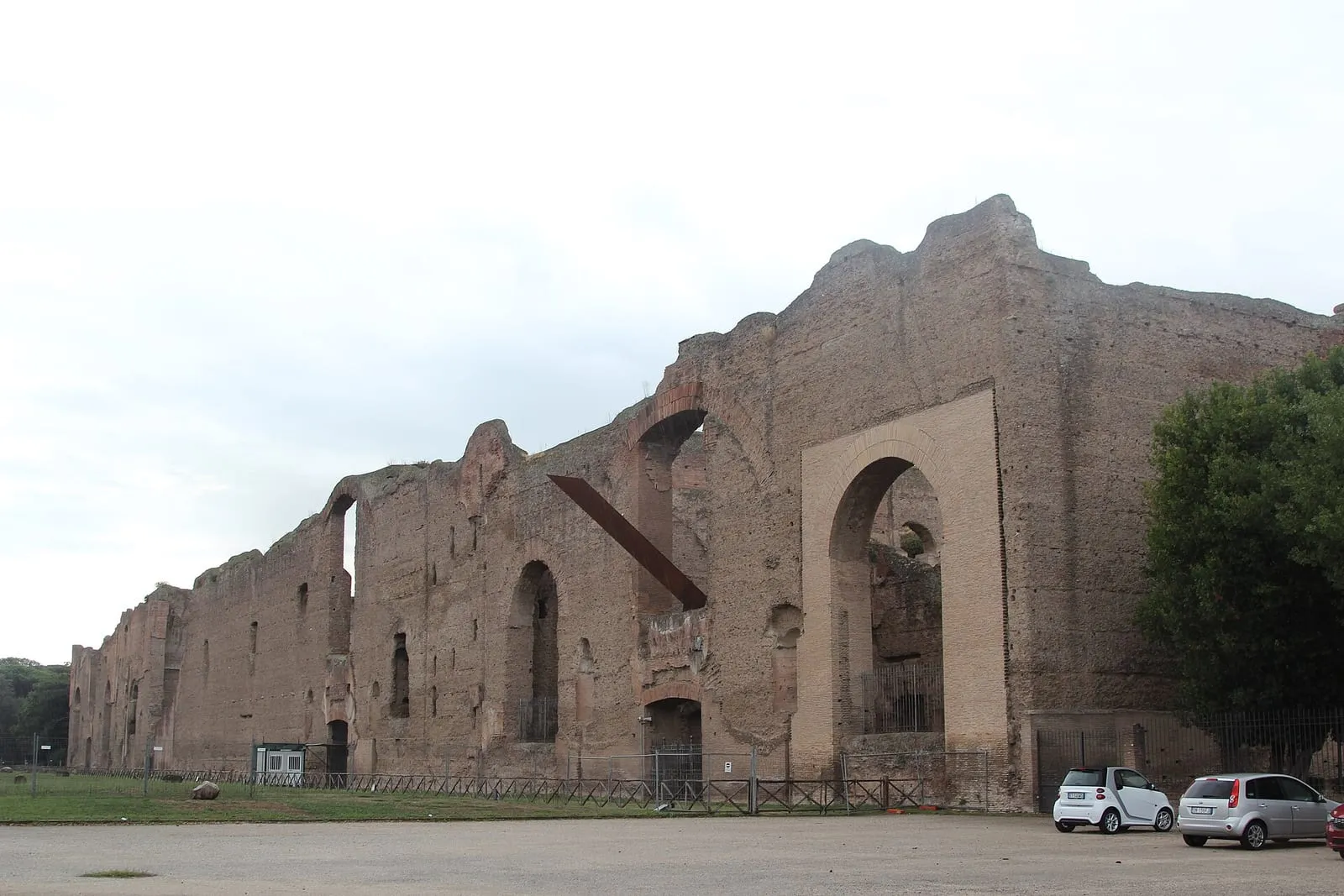 Hauts murs de brique des thermes de Caracalla à Rome, percés d'arcades, au-dessus d'une pelouse et d'une route