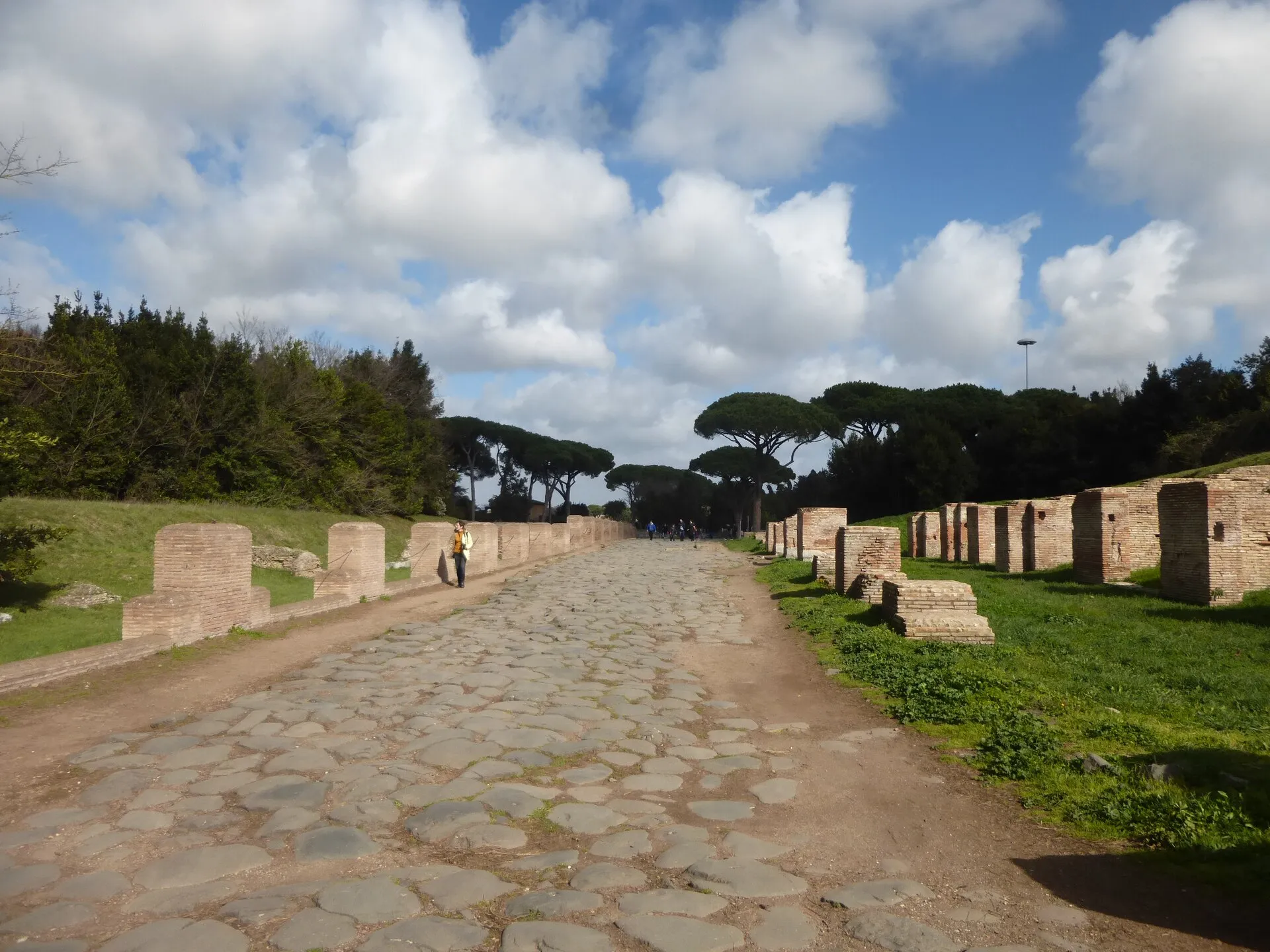 Le decumanus maximus d'Ostie Antica, large rue pavée de blocs de basalte bordée de ruines de brique et de pins parasols