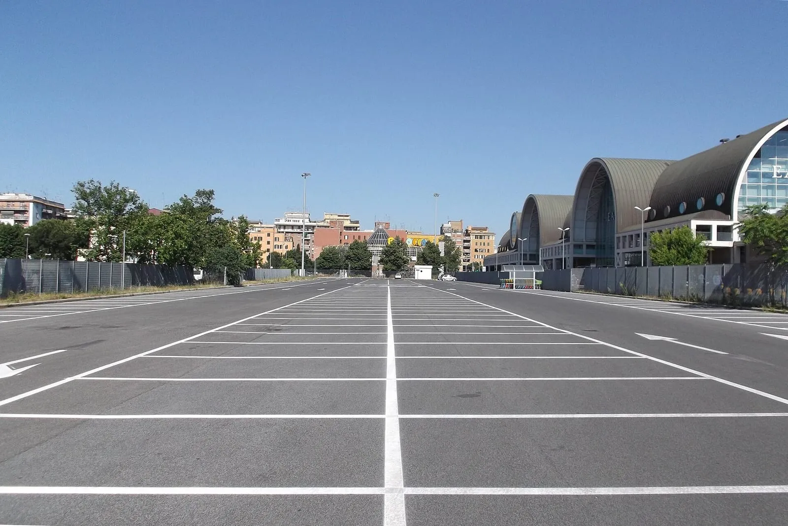Grand parking à ciel ouvert près de la gare Ostiense à Rome, marquages blancs au sol et bâtiment moderne