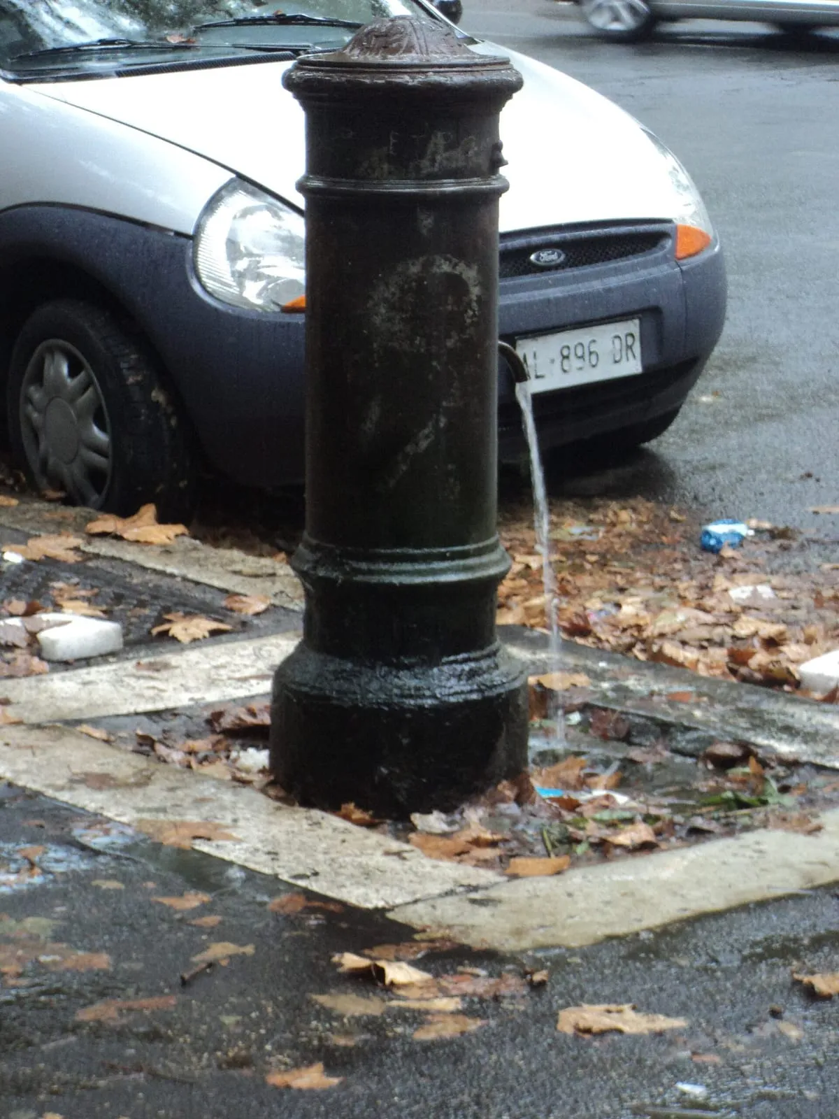 Fontaine publique en fonte de type nasone au bord d'une rue de Rome, son bec laissant couler un filet d'eau continu