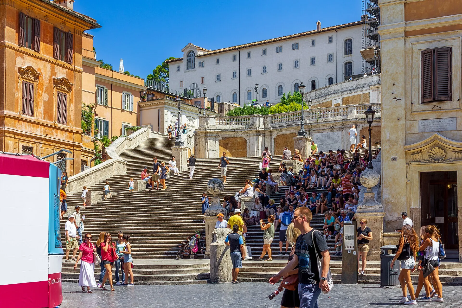 L'escalier de la Trinité-des-Monts à Rome, couvert de visiteurs par une journée ensoleillée, s'élève vers l'église Santissima Trinità dei Monti, avec la fontaine de la Barcaccia au premier plan