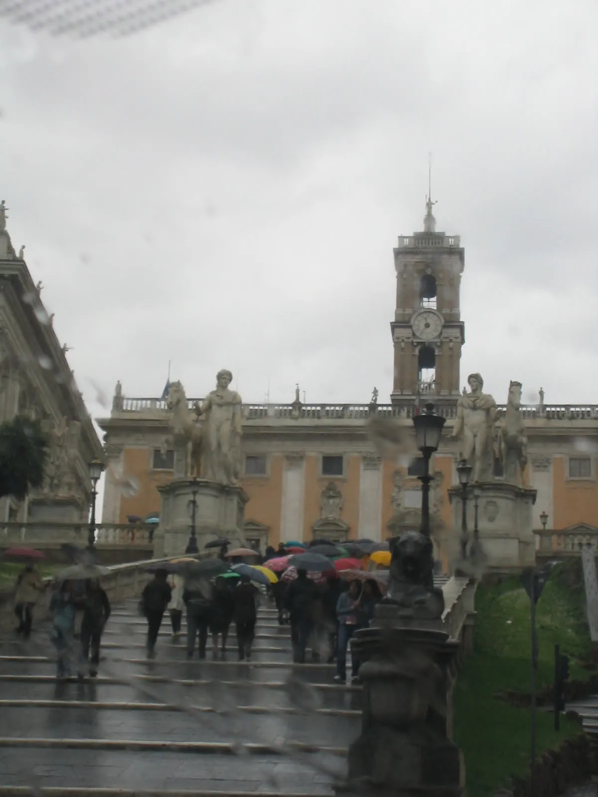 La Cordonata du Capitole sous une pluie battante, passants munis de parapluies montant les marches vers la place du Capitole à Rome