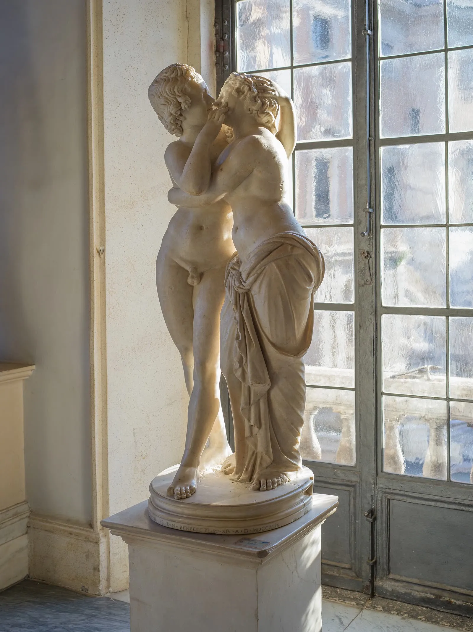 Le groupe sculpté d'Amore e Psiche en marbre, exposé dans une salle des musées du Capitole à Rome, devant une fenêtre