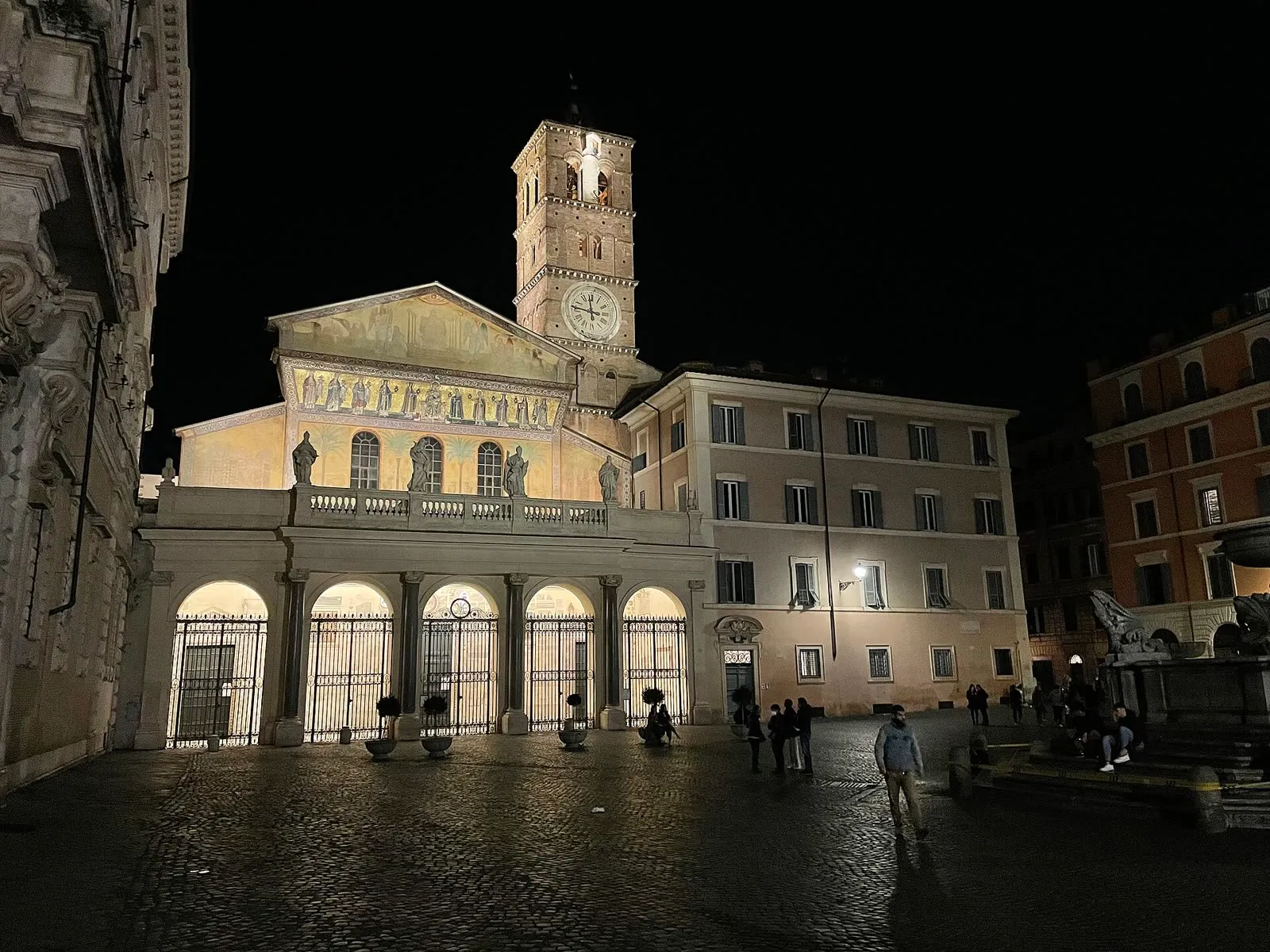La place Santa Maria in Trastevere à la nuit tombée, la mosaïque dorée et le campanile de la basilique éclairés, la fontaine octogonale et le pavé de sampietrini