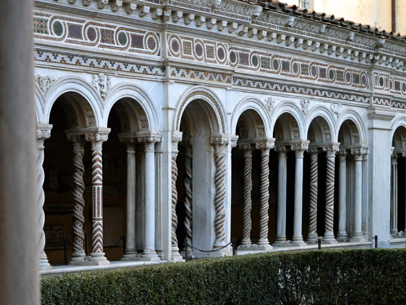 Dans le cloître cosmatesque, colonnettes géminées torsadées et bandeaux de marbre incrustés de mosaïques autour d'un parterre du jardin