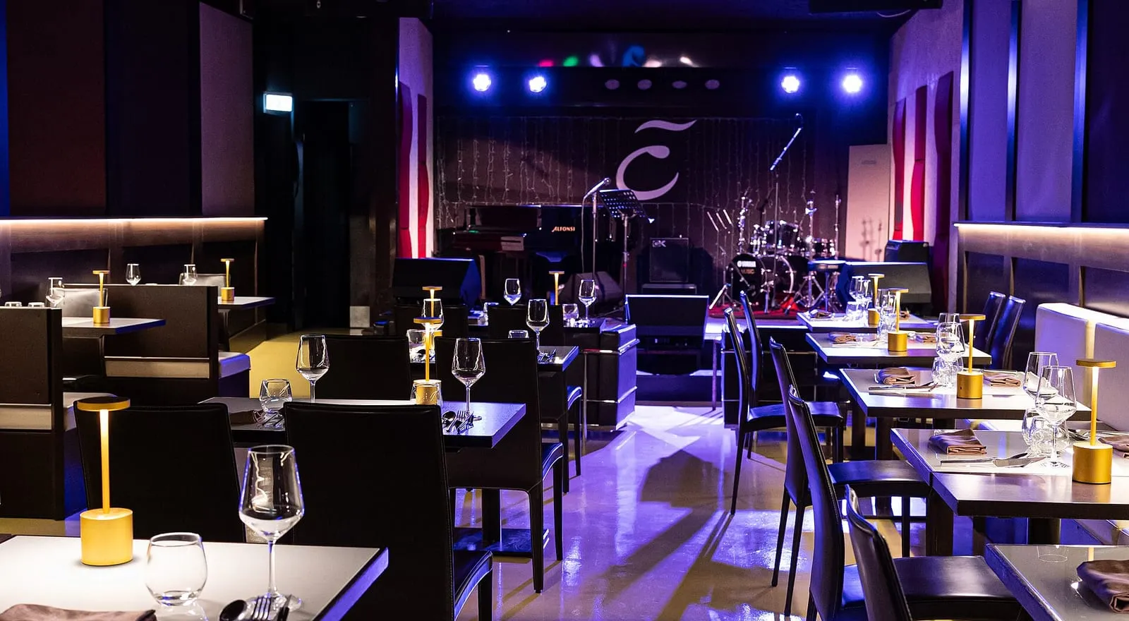Salle d'un club de jazz à Rome avec sa scène, une batterie et un clavier, tables dressées et lumière bleue