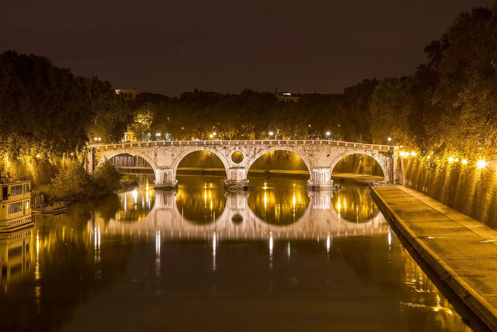 Le Ponte Sisto illuminé la nuit au-dessus du Tibre, reflets jaunes dans l'eau