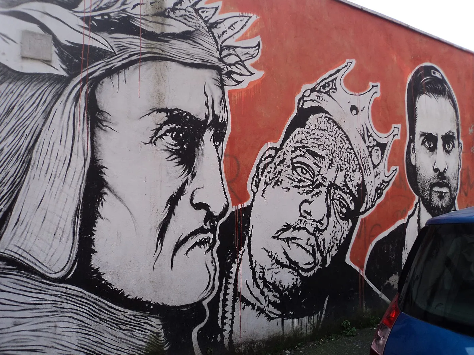 Visages stylisés en noir et blanc peints sur un mur rouge vif, fresque du quartier Ostiense à Rome