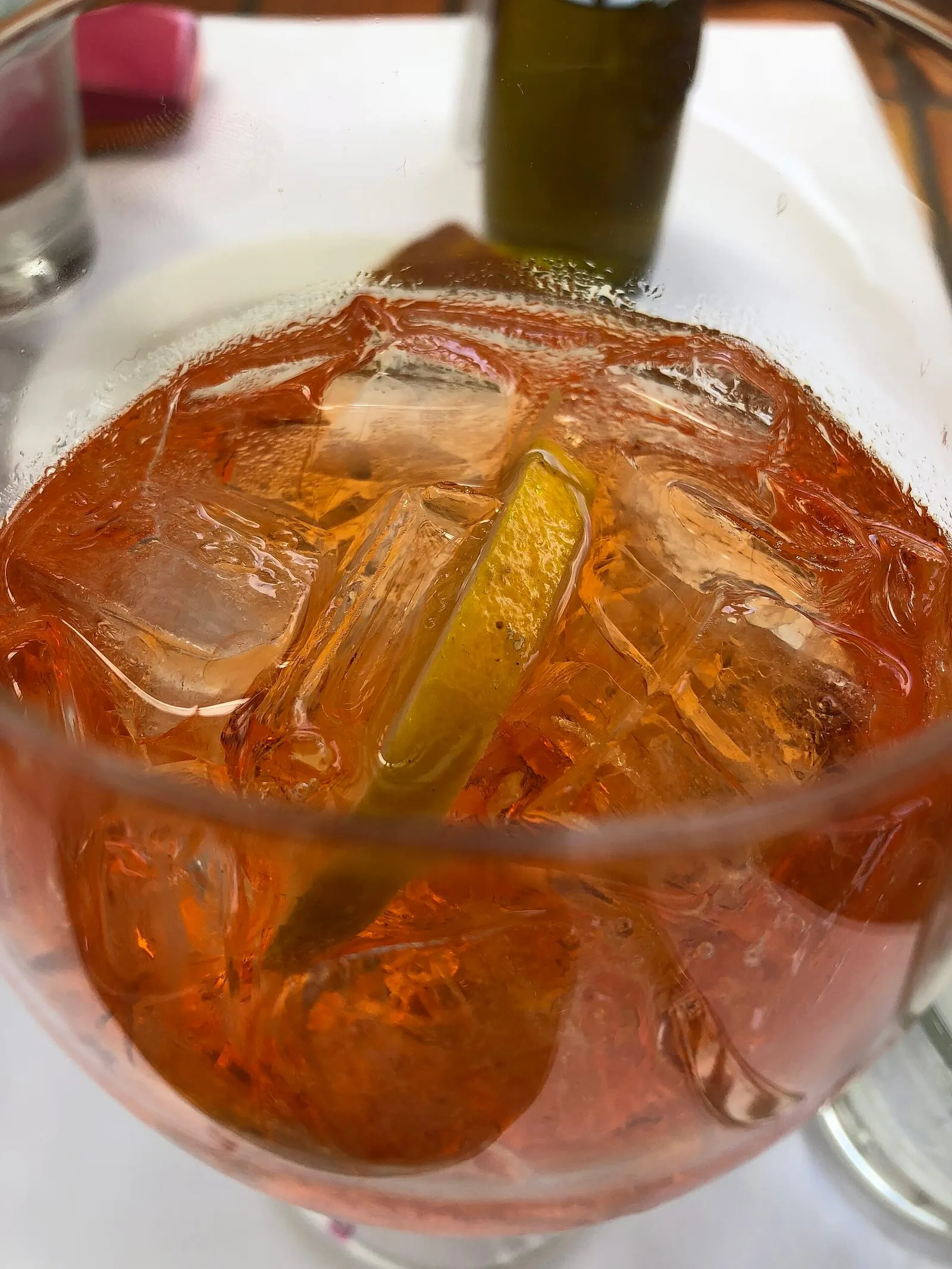 Un spritz ambré servi dans un grand verre à pied, garni d'un quartier de citron vert et de glaçons, sur une table de restaurant