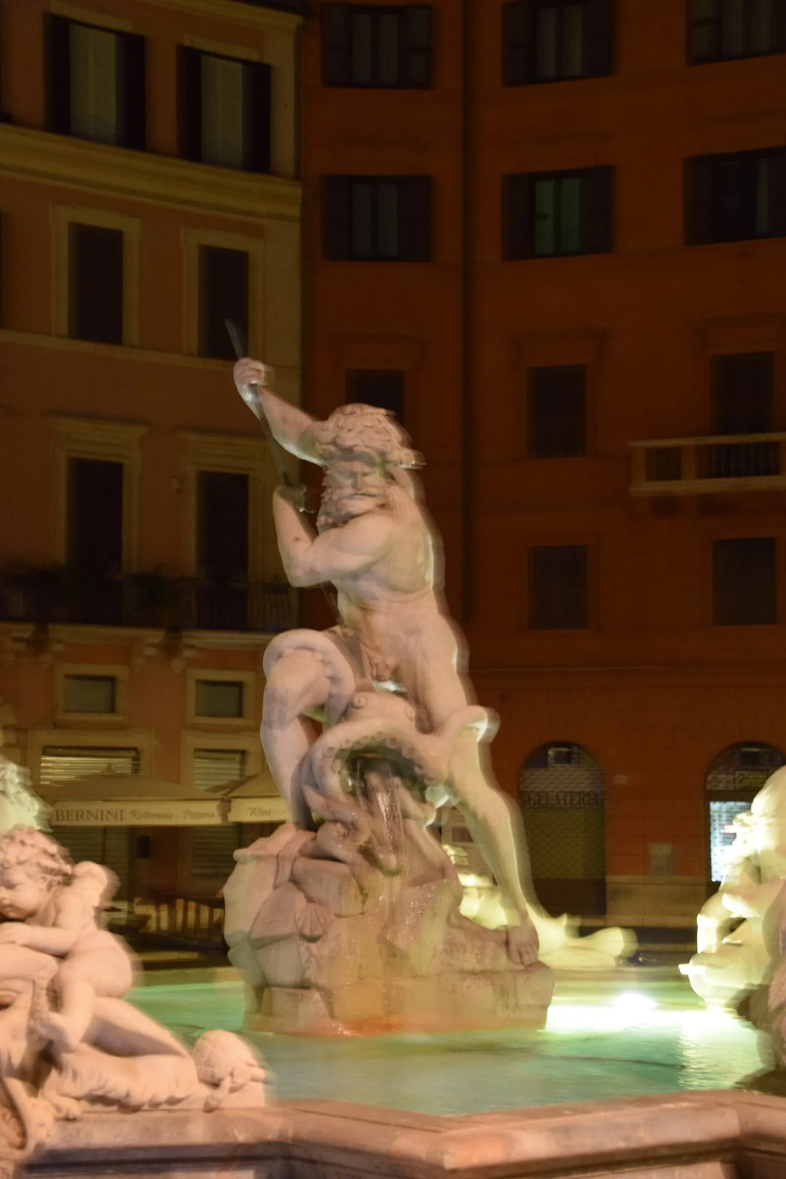 La fontaine de Neptune de la piazza Navona à Rome, sa statue de marbre et sa vasque éclairées la nuit devant les façades ocre de la place