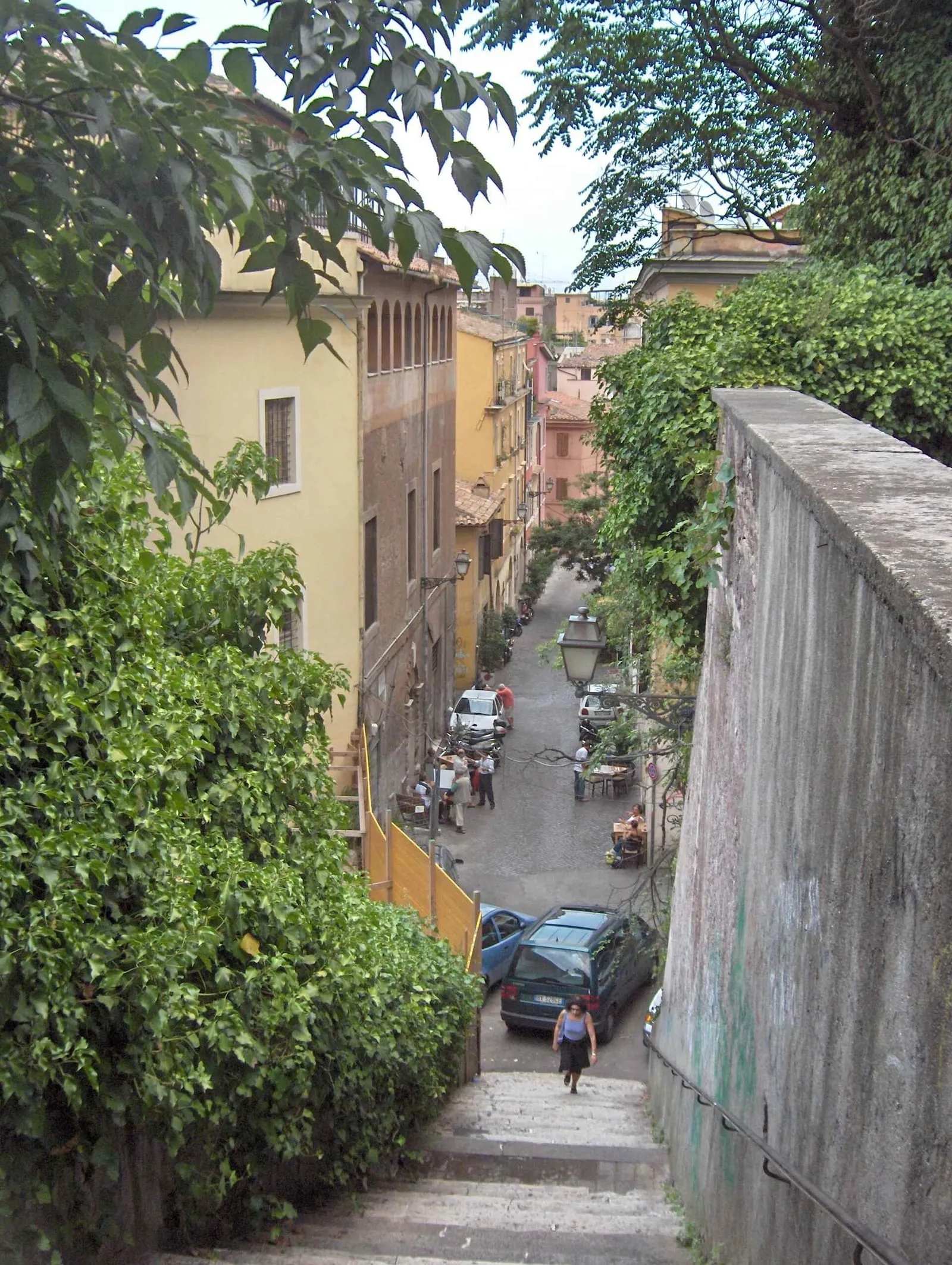 Ruelle en pente du Trastevere à Rome, pavée et bordée de façades ocre avec volets de bois, vue depuis un escalier envahi de verdure