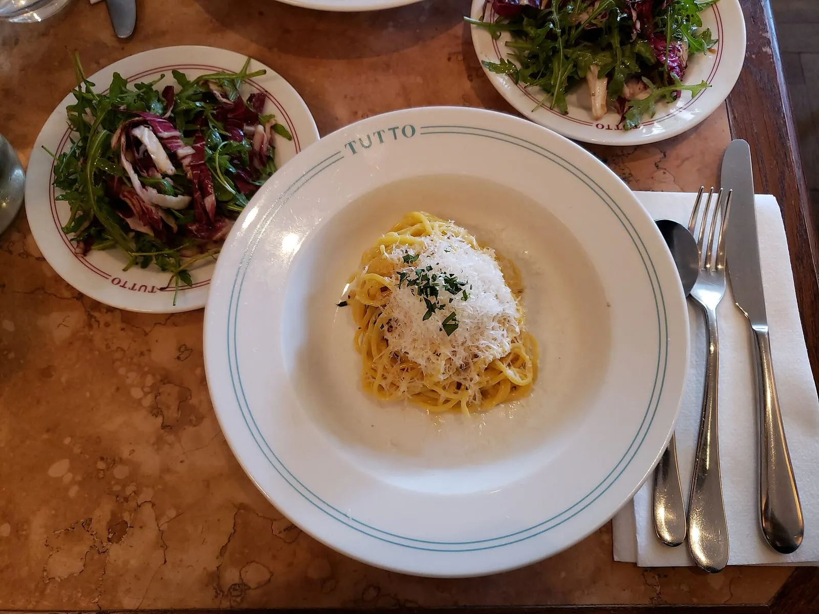 Assiette de spaghetti cacio e pepe au pecorino râpé et au poivre, servie avec une salade de chicorée